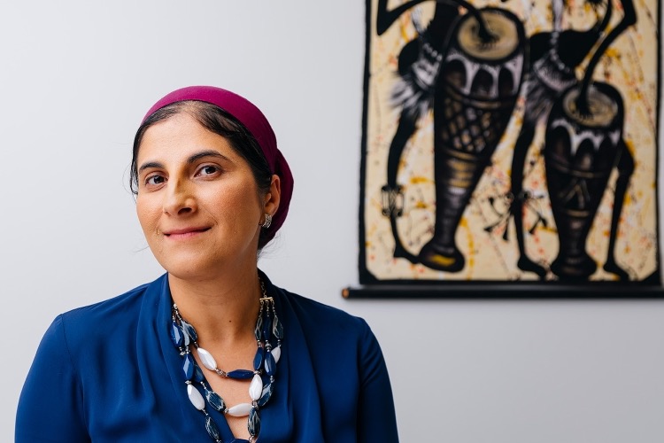 Supreet Kaur in her office, in front of a batik wall hanging of drummers